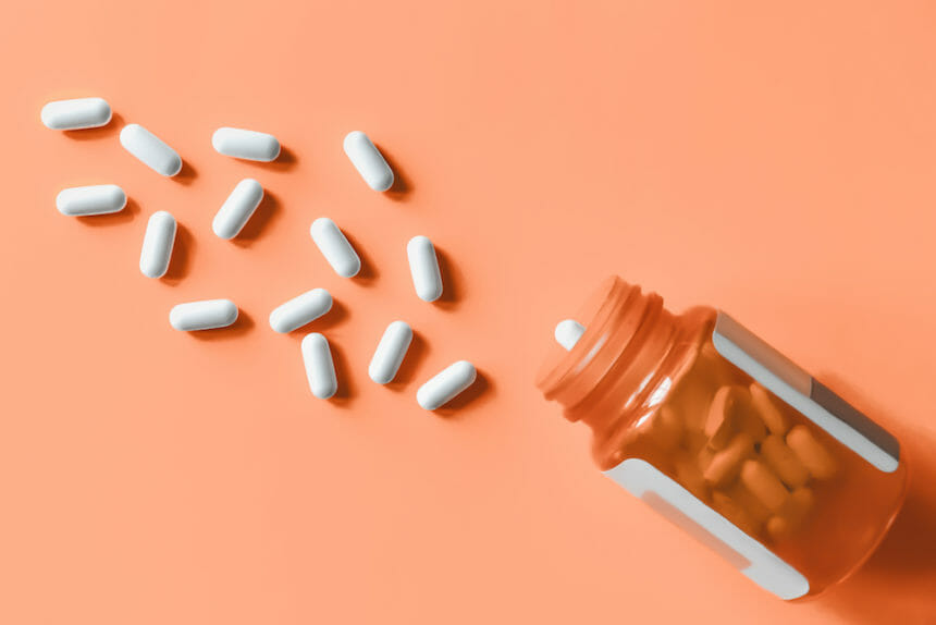 White pills spilling out of prescription bottle onto orange surface