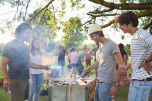 Happy adult friends barbecuing at sunset party in park