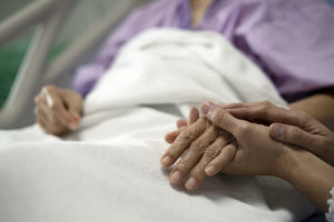 Image of daughter holding the mother's hand and encourage while her mother sitting on bed in hospital.
