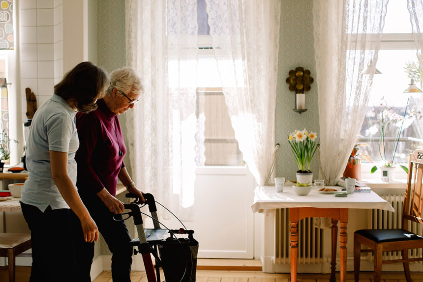 Side view of female healthcare worker assisting elderly woman with rollator in nursing home