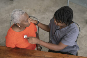 A young nurse wearing medical scrubs checks a senior patients heart rate. This is an in-house patient visit.