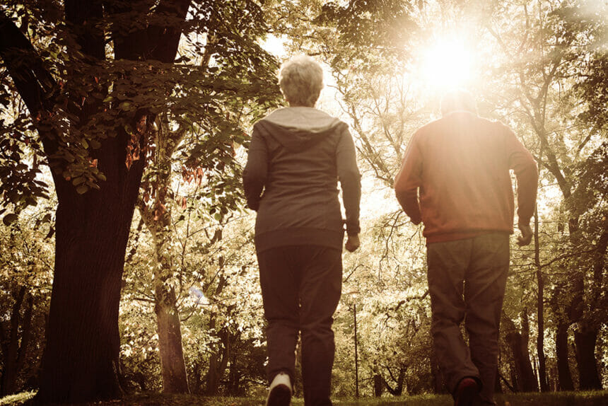 Active senior woman and man jogging trough park together. From back.