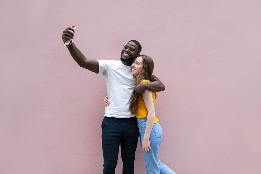 A young man taking a selfie with girlfriend with a pink background