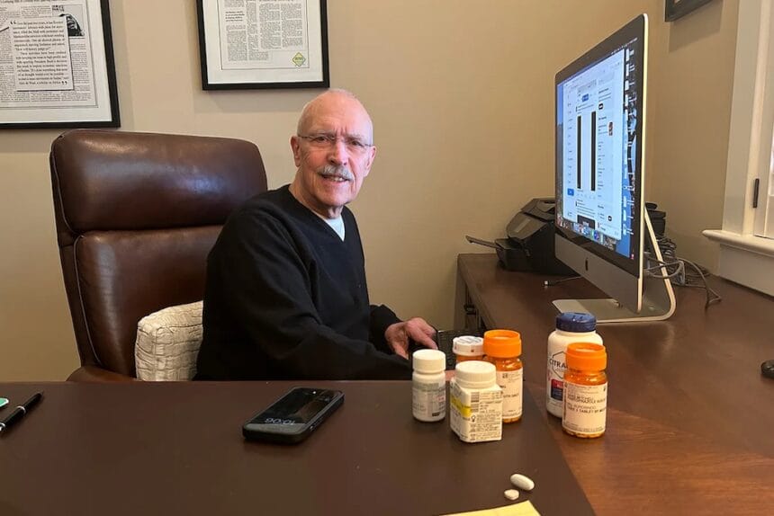 David Mitchell, founder of Patients for Affordable Drugs, sits in his home office. Beside him are some of the many drugs he takes to treat multiple myeloma and other conditions