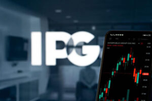 IPG's logo, slightly out of focus, and a smartphone screen in the foreground with a financial performance graphic
